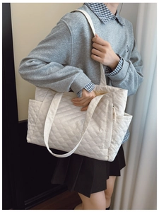 Close-up of quilted tote bag side pocket and stitching detail on white shoulder bag