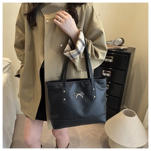 Detail of black PU leather tote bag featuring gold metallic bow and rivet accents