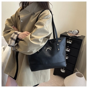Detail of black faux leather tote bag with silver metal bow and long shoulder strap
