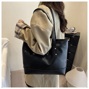 Detail of black tote bag featuring delicate lychee grain texture and a metal bow accent