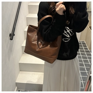 Detail of a brown leather tote bag with metal bow buckle and rivets on white stairs