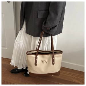 Detail of a minimalist cream and brown tote bag with a golden bow and metal rivets