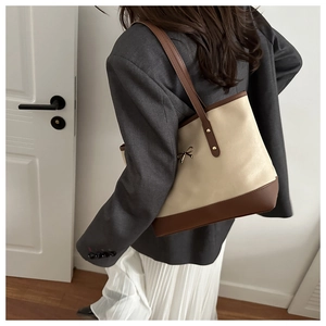Detail of a chic cream and brown tote bag with metal bow accent on model in a suit