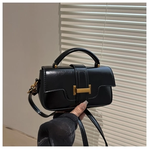 Detail of black mini handbag featuring a golden rectangular lock and pebbled leather texture