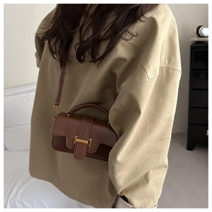 Sac à bandoulière en cuir marron avec fermoir métallique porté par un mannequin