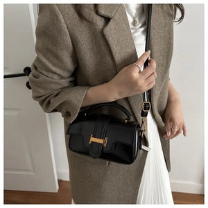 Detail of black leather handbag with gold H-buckle and adjustable shoulder strap