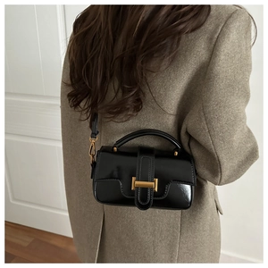 Détail d'un sac à bandoulière en cuir noir brillant avec des finitions dorées sur un manteau