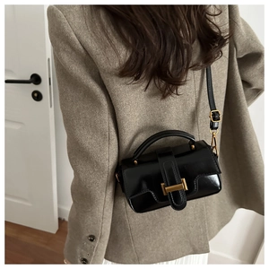 Détail du sac bandoulière noir brillant avec boucle dorée porté par un mannequin en tailleur