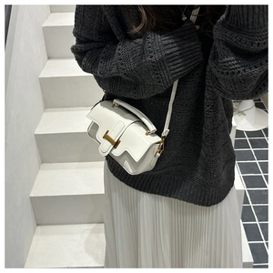 On-body view of a white leather crossbody bag with a gold metal clasp and handle