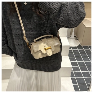 Detail of beige oil leather crossbody bag with gold buckle on a model wearing knitwear