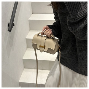 Detail of a minimalist beige leather handbag featuring a golden H-clasp and top handle