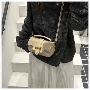 Sac bandoulière crème avec fermoir en H doré porté par un mannequin en tenue chic