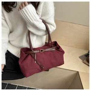 Detail of burgundy suede tote bag featuring brown leather straps and gold metal buckles
