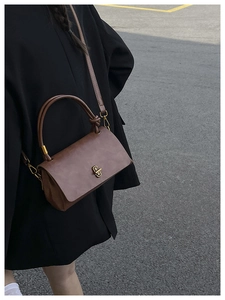 Detail of vintage brown leather handbag with gold twist lock worn by a model in black coat