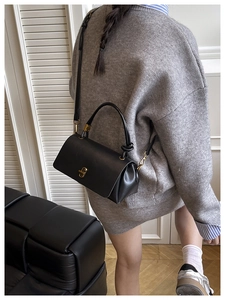 Detailed view of a black leather handbag with gold metal lock on a model outfit