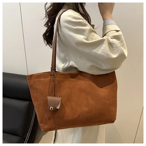 Detail of a large brown suede tote bag featuring a leather strap and mini pouch charm