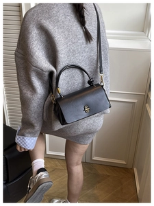 Model wearing black crossbody bag with gold buckle in home setting detail shot