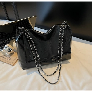 Detail of black glossy patent leather chain bag with natural pleated texture and silver strap