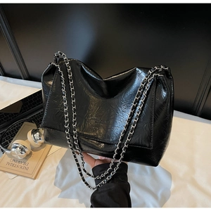 Close-up of black glossy wrinkled texture and silver metal chain strap on tote bag
