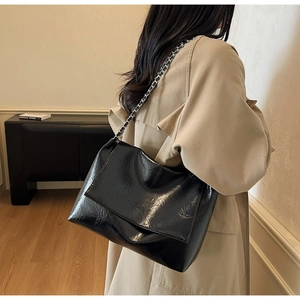 Detail of glossy black chain shoulder bag with crinkled texture on a beige coat