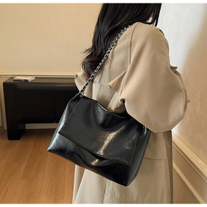 Close-up of a glossy black leather shoulder bag with a silver chain strap on a model