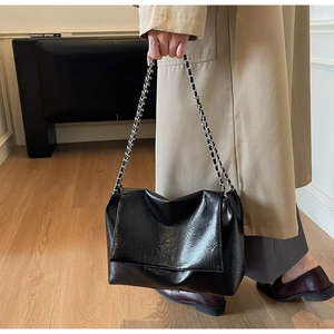 Detail of glossy wrinkled leather texture and chain strap on black tote shoulder bag