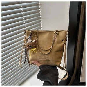 Detail of khaki suede bucket bag with drawstring closure and cute teddy bear charm