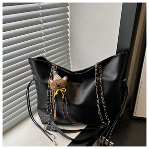 Close-up of black leather tote with gold logo and cute bear charm on a windowsill