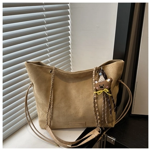 Detail of suede tote bag featuring braided chain strap and cute brown bear pendant