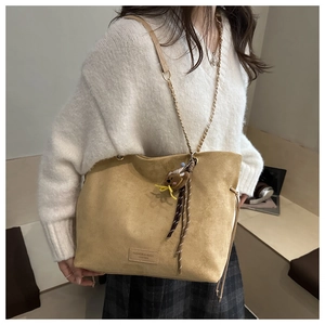 Detail of khaki suede shoulder bag with chain strap and cute bear keychain accessory