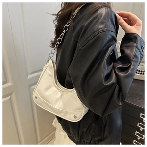 Detail view of white glossy crescent bag with silver chain strap on a black jacket