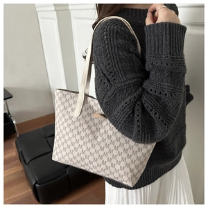 Close-up of the vintage monogram pattern and sleek metal detail on an off-white tote bag