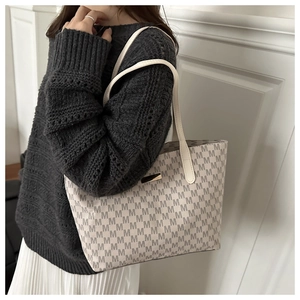 Detail of a beige letter M printed tote bag styled with a grey knitted sweater