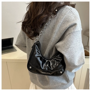 Detail of black patent leather underarm bag with silver chain strap and metal rivets