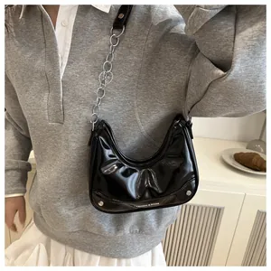 Detail of black patent leather crescent bag with metal chain strap and rivet hardware