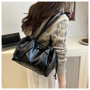 Elegant black glossy shoulder bag featuring a decorative bow and chic drawstring detail