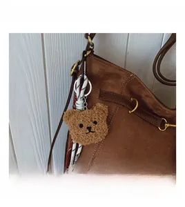 Brown teddy bear plush charm with woven rope detail on a brown suede tote bag