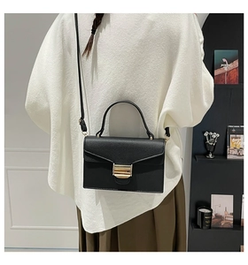 Détail du sac à main en cuir noir grainé avec boucle dorée porté par un mannequin