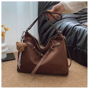 Dettaglio borsa tote in pelle scamosciata marrone scuro con cinturino e ciondolo orso