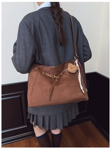 Detail of deep brown suede tote bag featuring cross straps and plush bear charm decoration