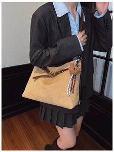 Detail of light khaki suede tote bag with brown leather straps and plush bear charm