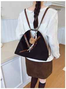 Close-up of a black triangular backpack with brown straps and a cute plush bear charm