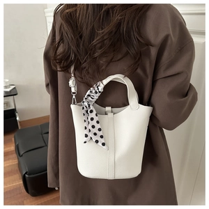 Minimalist white lychee leather bucket bag with a silk scarf tied on the top handles