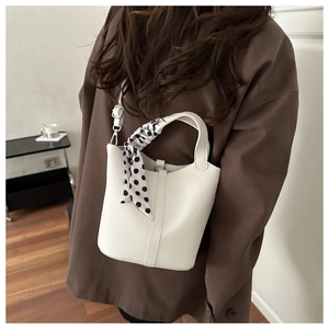 Detailed view of white bucket bag with polka dot scarf on handle worn by model