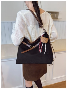Close-up of a large coffee brown suede shoulder bag with a cute plush bear charm