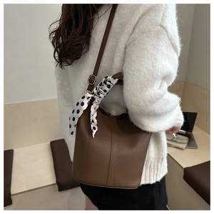 Detail of dark brown lychee texture leather bucket bag with silk scarf on the handle
