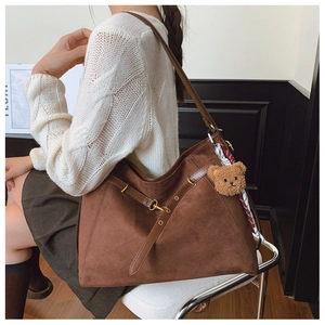 Detailed view of brown suede tote bag with leather straps and plush bear charm