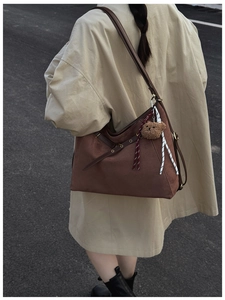 Dettaglio della borsa tote in pelle scamosciata marrone scuro con occhielli e ciondolo orso