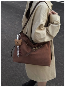 Detail of dark brown suede shoulder bag with leather straps and cute bear pendant charm