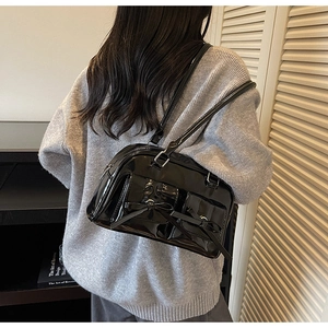 Detail of glossy black patent leather bag with bow pockets and silver hardware